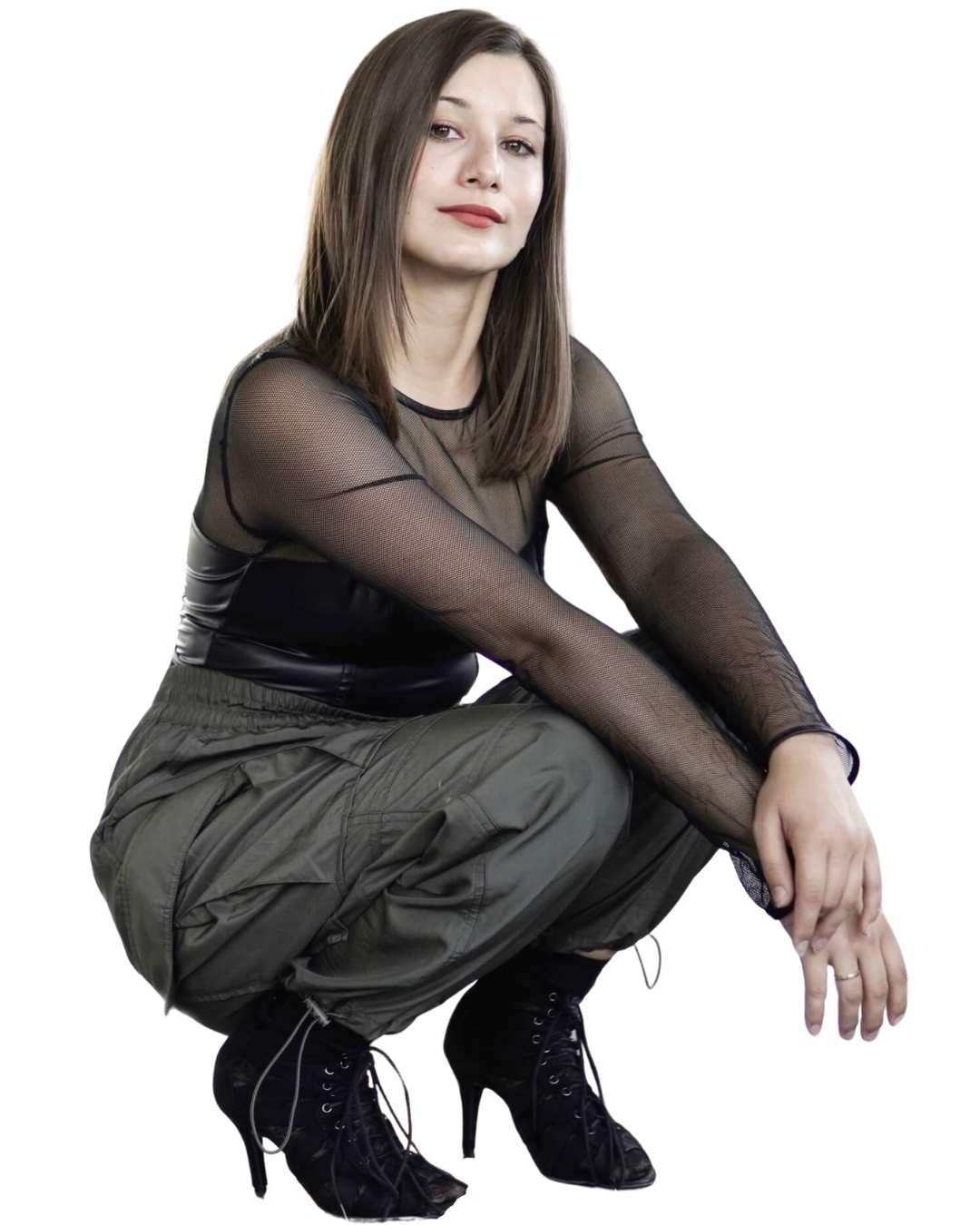 Tänzerin in schwarzem Netz-Top und Cargohose in Hocke-Pose mit High Heels vor weißem Hintergrund.