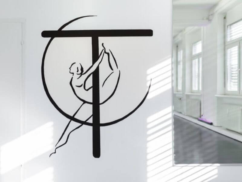 Wandgestaltung im Studio T-Tanzstück mit einem stilisierten Logo: Eine Figur an einer vertikalen Pole, integriert in ein großes „T“ und einen Kreis.